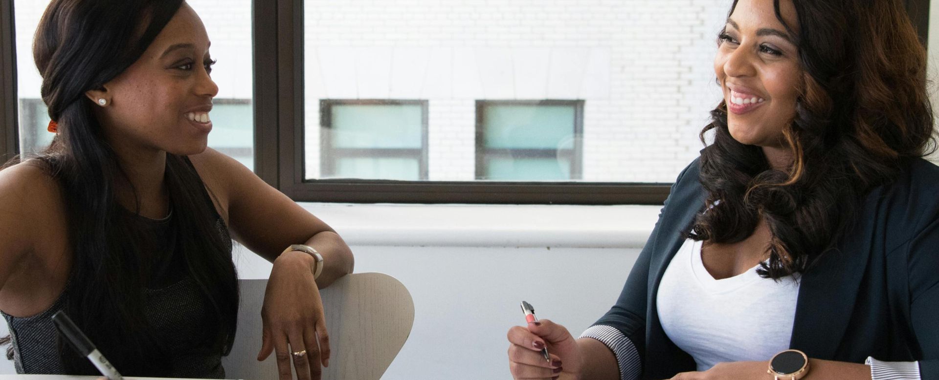 Two smiling businesswomen having a meeting in a bright office space, taking notes and discussing ideas.