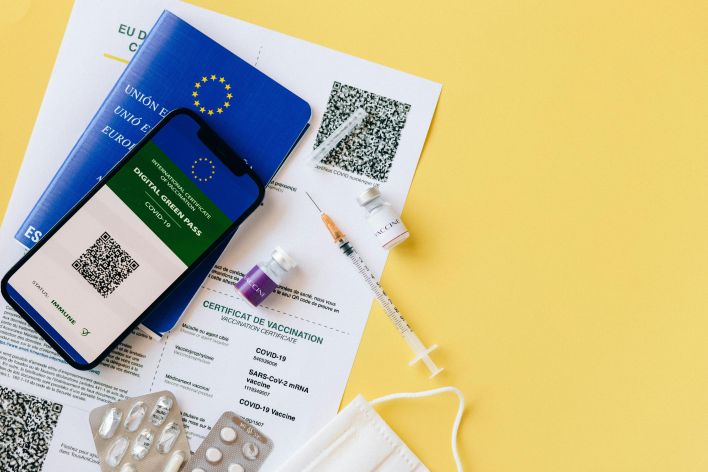 Digital vaccine passport and COVID-19 vaccination items including syringes and masks on a yellow background.