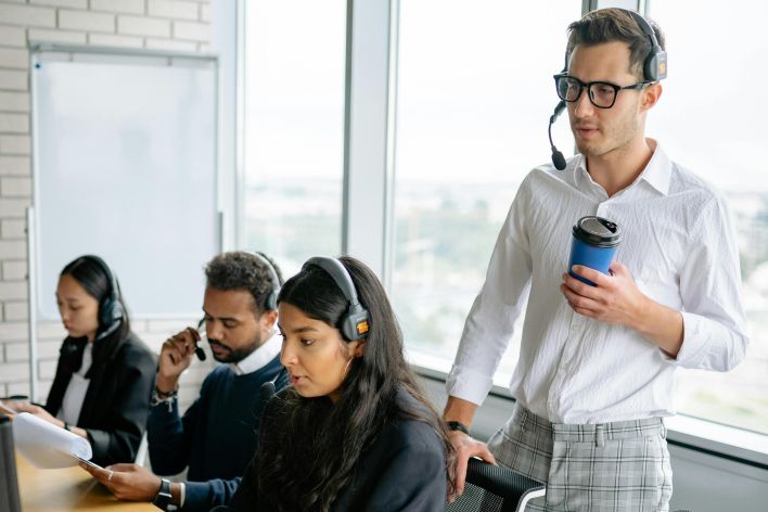 Diverse call center team working together in a modern office setting, using headsets and computers.