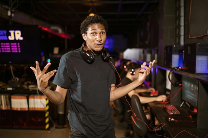 Smiling young man with headphones in a gaming café, embodying confidence and casual style.